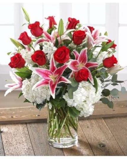 Arrangement of red roses, pink lilies, and white hydrangeas in a clear glass vase