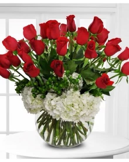 Round vase of red roses arranged above white hydrangeas in a clear glass bowl