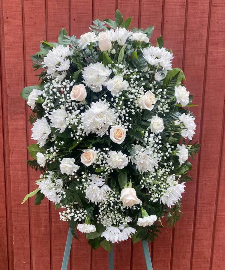 Oval standing spray of white flowers and ivory roses on an easel.
