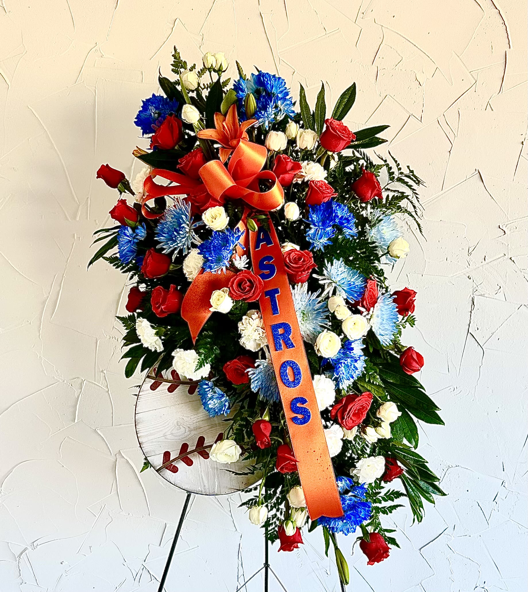 Tall standing spray of red, blue, and white flowers with orange ASTROS ribbon and baseball sign on an easel