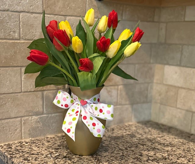 Red and yellow tulips in a gold vase with a white polka dot bow on a countertop