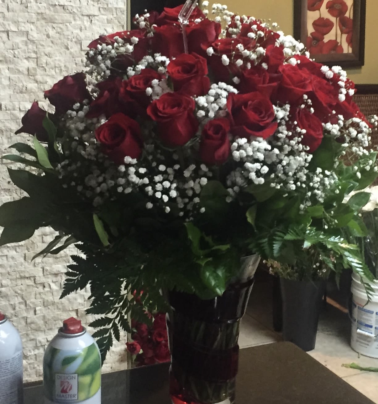 Large bouquet of red roses and white filler flowers in a tall dark glass vase