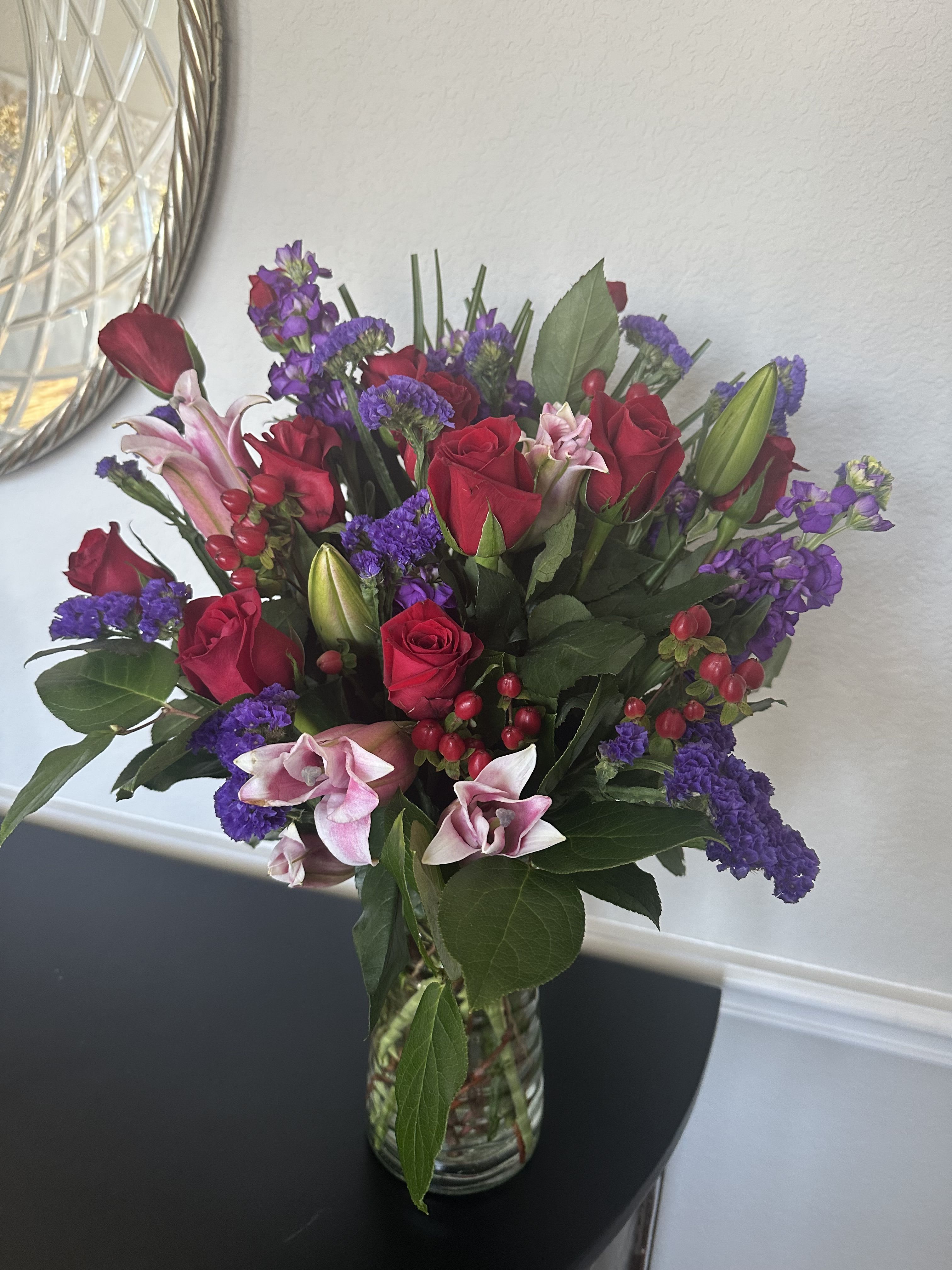 Bouquet of red roses, pink lilies, and purple flowers in a clear glass vase