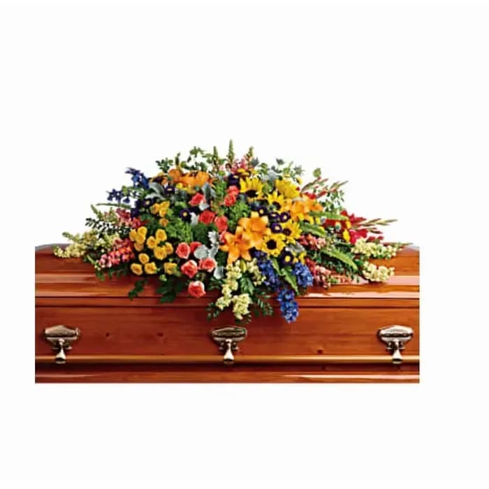 Colorful mixed flower casket spray with yellow, orange, blue, and pink blooms on a wooden casket