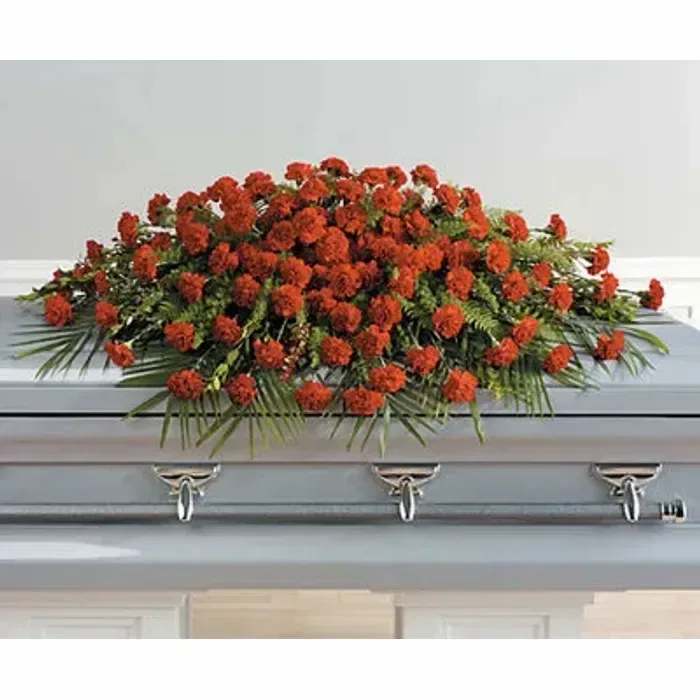Red carnation casket spray with palm fronds draped over a light gray casket