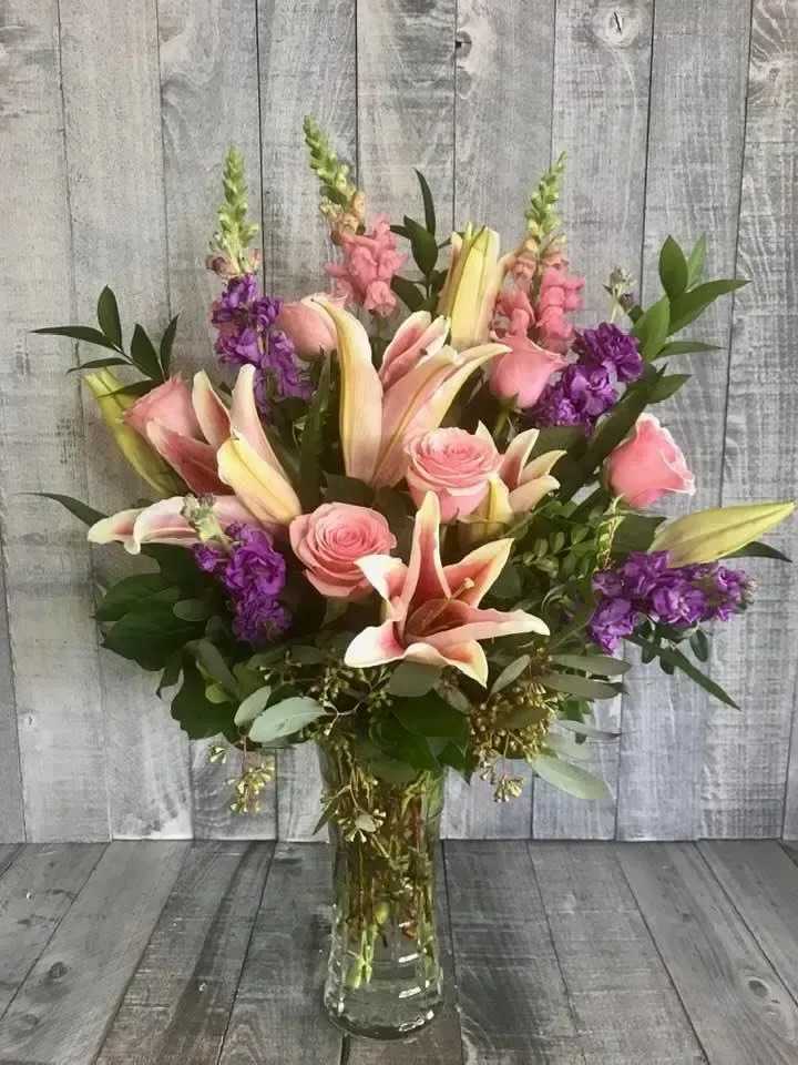 Tall mixed bouquet of pink lilies, pink roses, and purple flowers in a clear glass vase