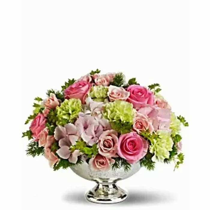 Low round arrangement of pink roses, green blooms, and pale hydrangeas in a silver pedestal bowl
