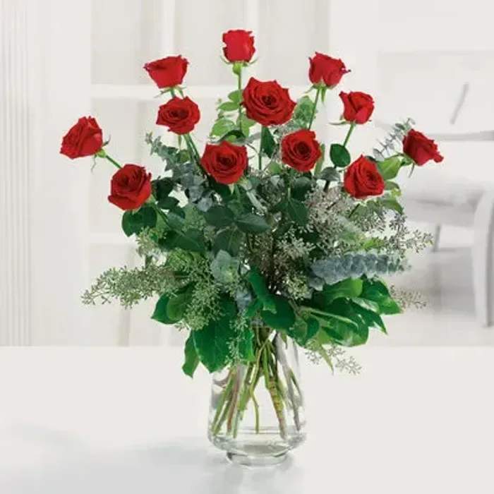 Tall arrangement of long-stem red roses with lush greenery in a clear glass vase