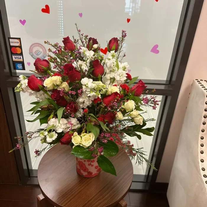 Tall arrangement of red roses, white flowers, and cream spray roses in a patterned ceramic vase