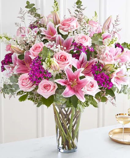 Tall glass vase filled with pink lilies, pink roses, and white and purple filler flowers