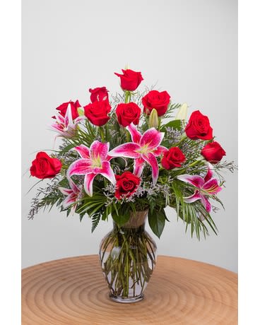 Tall arrangement of red roses and pink lilies in a clear glass vase