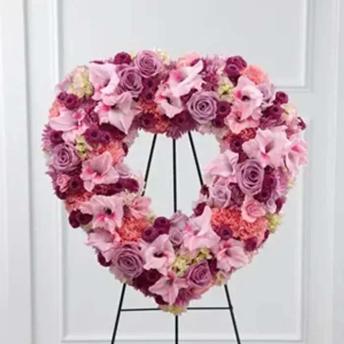 Heart-shaped floral wreath in pink and purple tones on a black stand