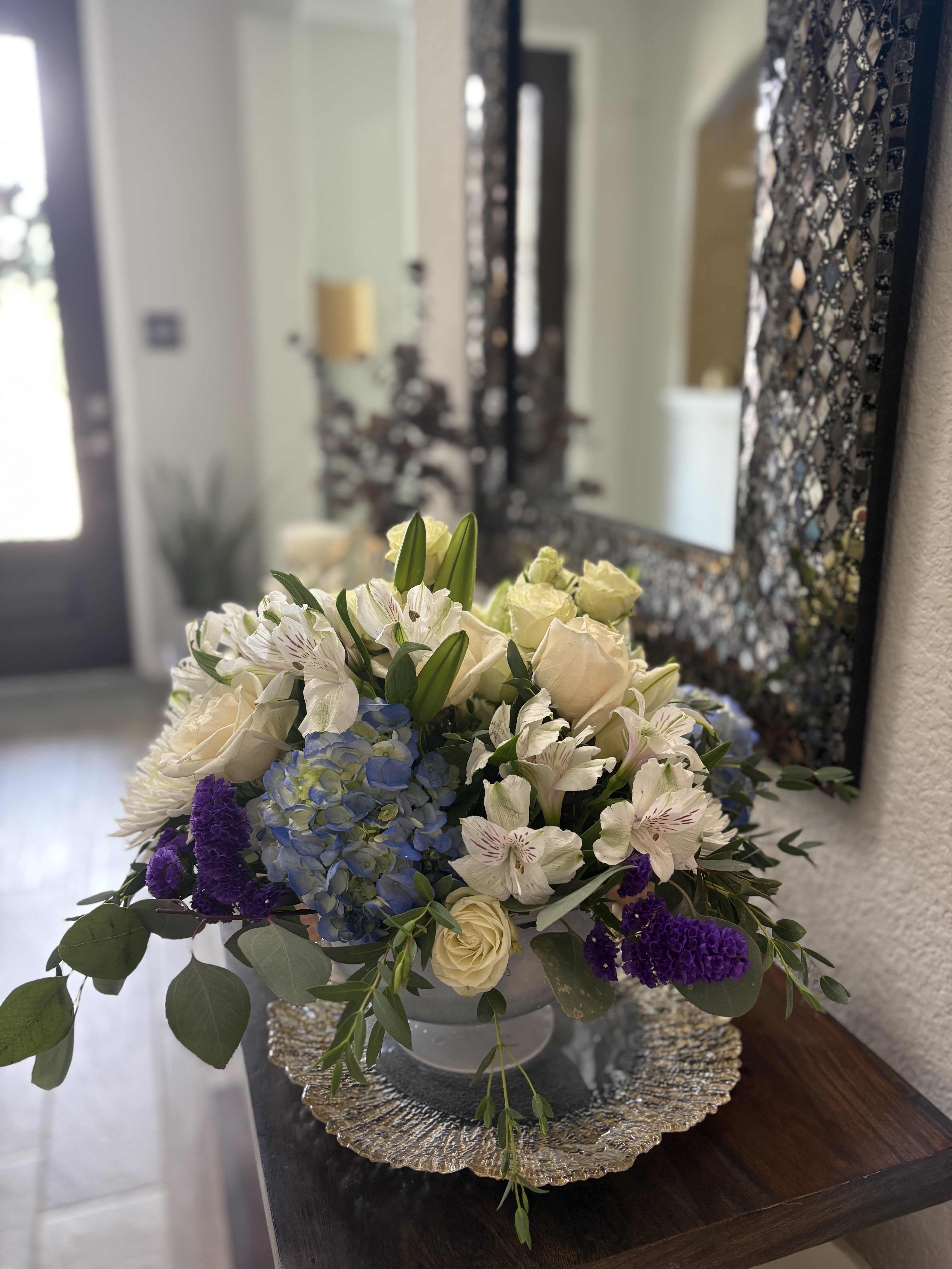 Mixed bouquet in a low silver bowl with cream, blue, and purple flowers