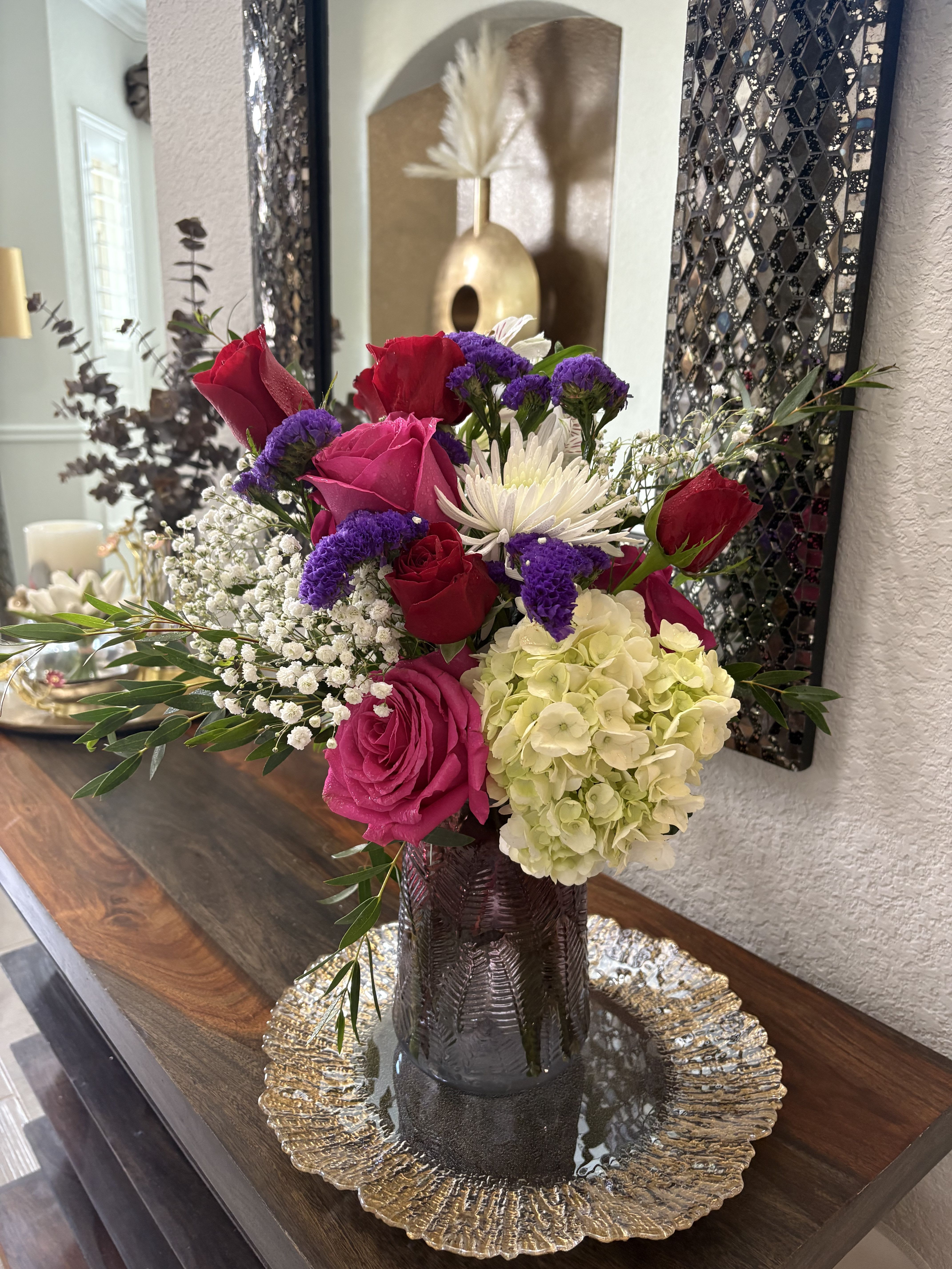 Mixed bouquet of roses, hydrangea, and white daisy-like blooms in a dark vase