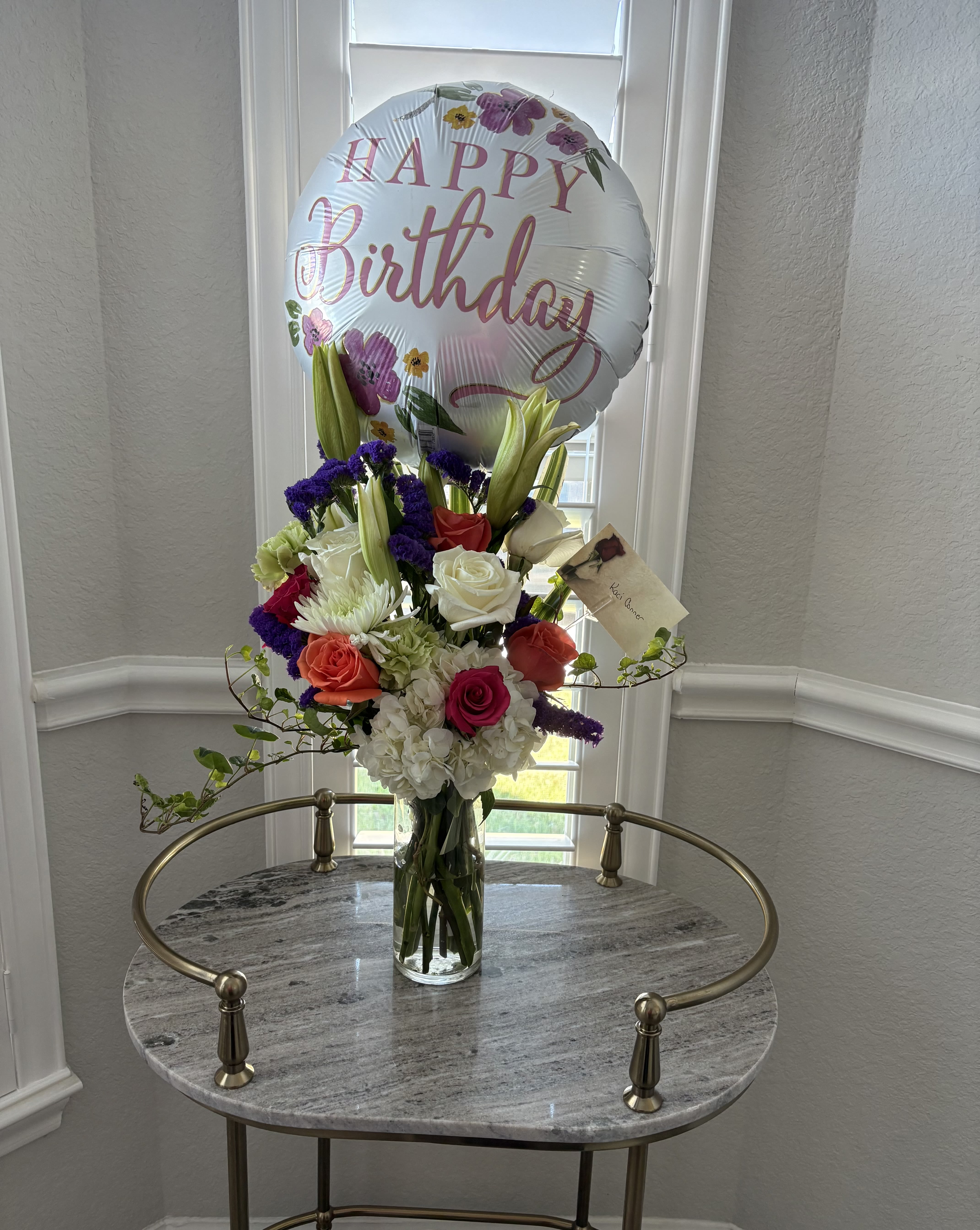 Birthday balloon above a mixed flower arrangement in a glass vase