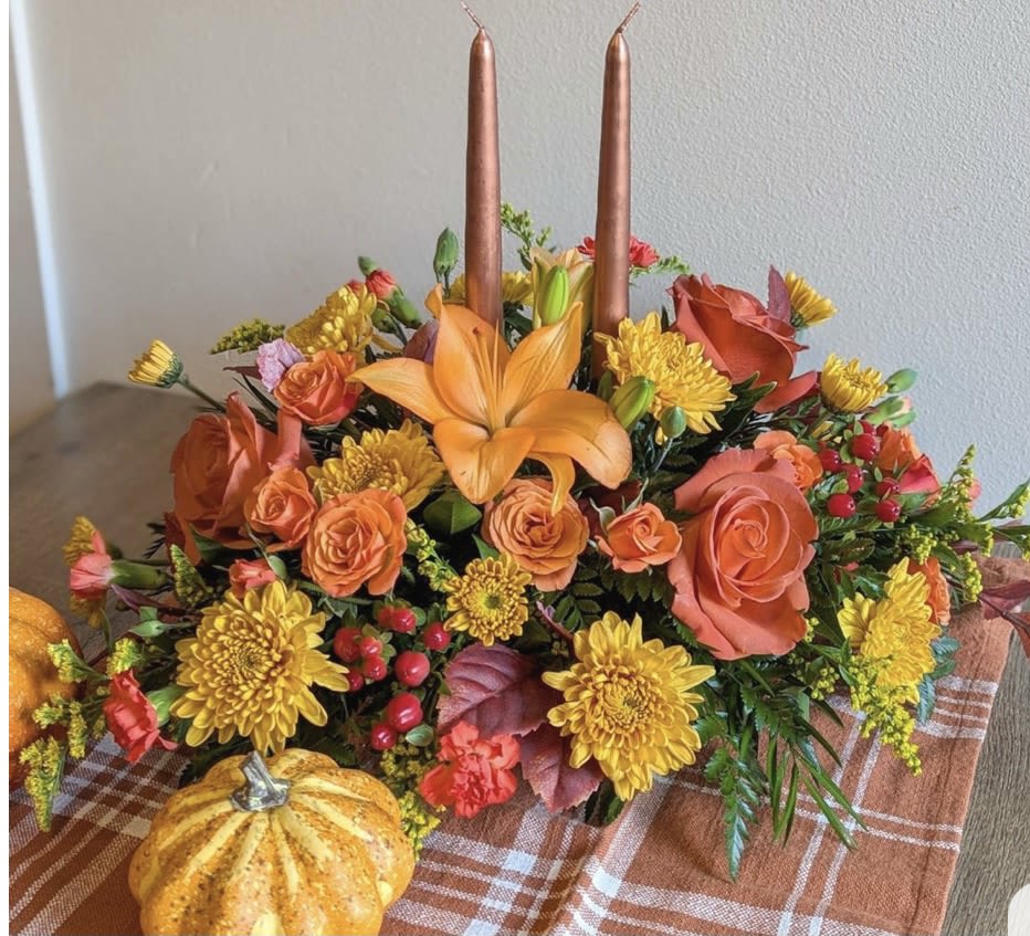 Autumn floral centerpiece with orange lilies, roses, and yellow mums around two candles