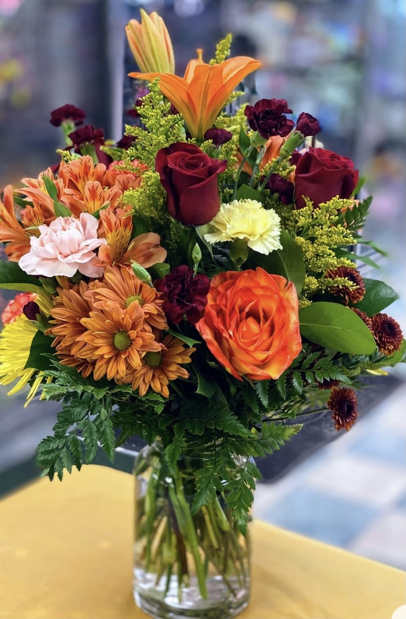 Mixed bouquet of orange, red, and pink flowers in a clear glass vase