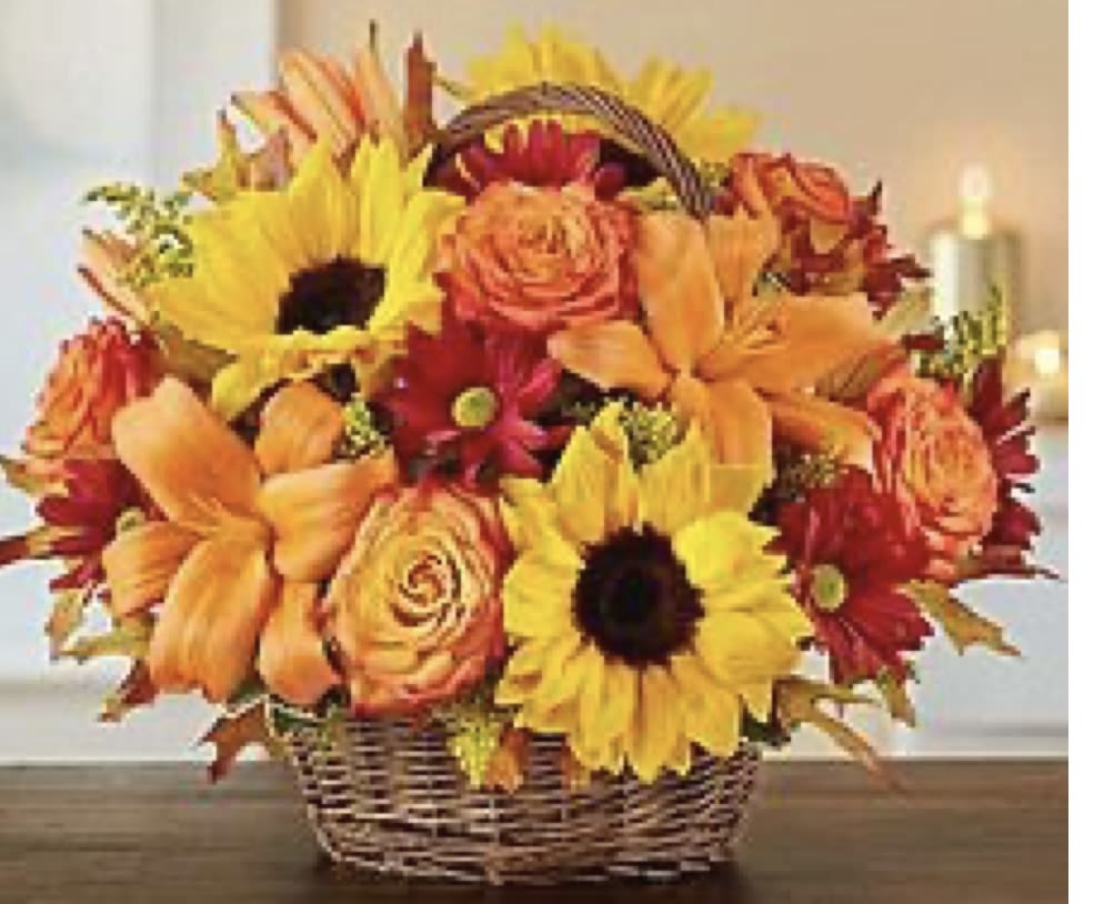 Basket arrangement of sunflowers, lilies, and roses in orange and yellow tones