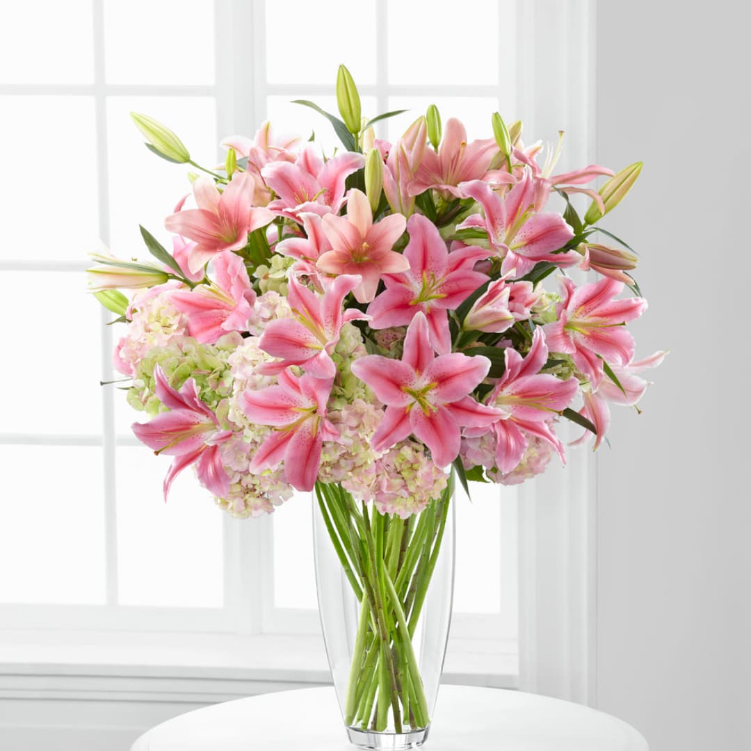 Pink lilies and pale hydrangeas in a clear glass vase