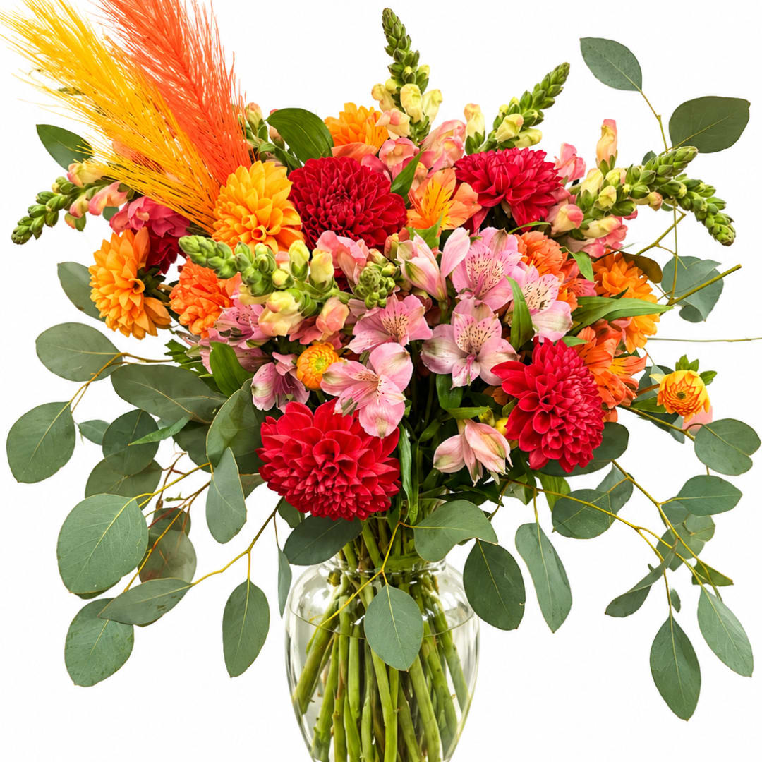 Bright mixed bouquet of red, pink, orange, and yellow flowers in a glass vase