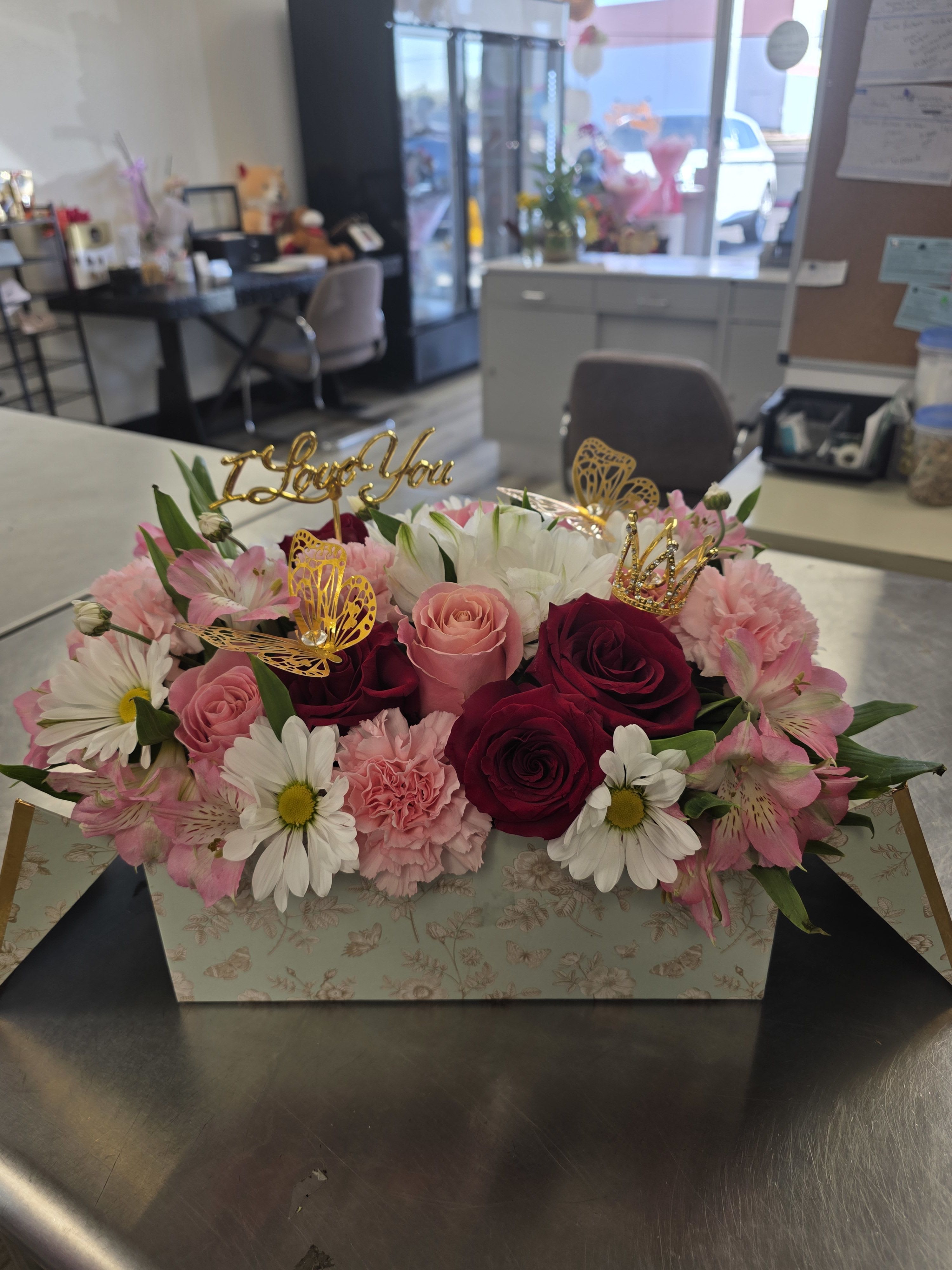 Pink and white flower arrangement in a floral box with gold toppers