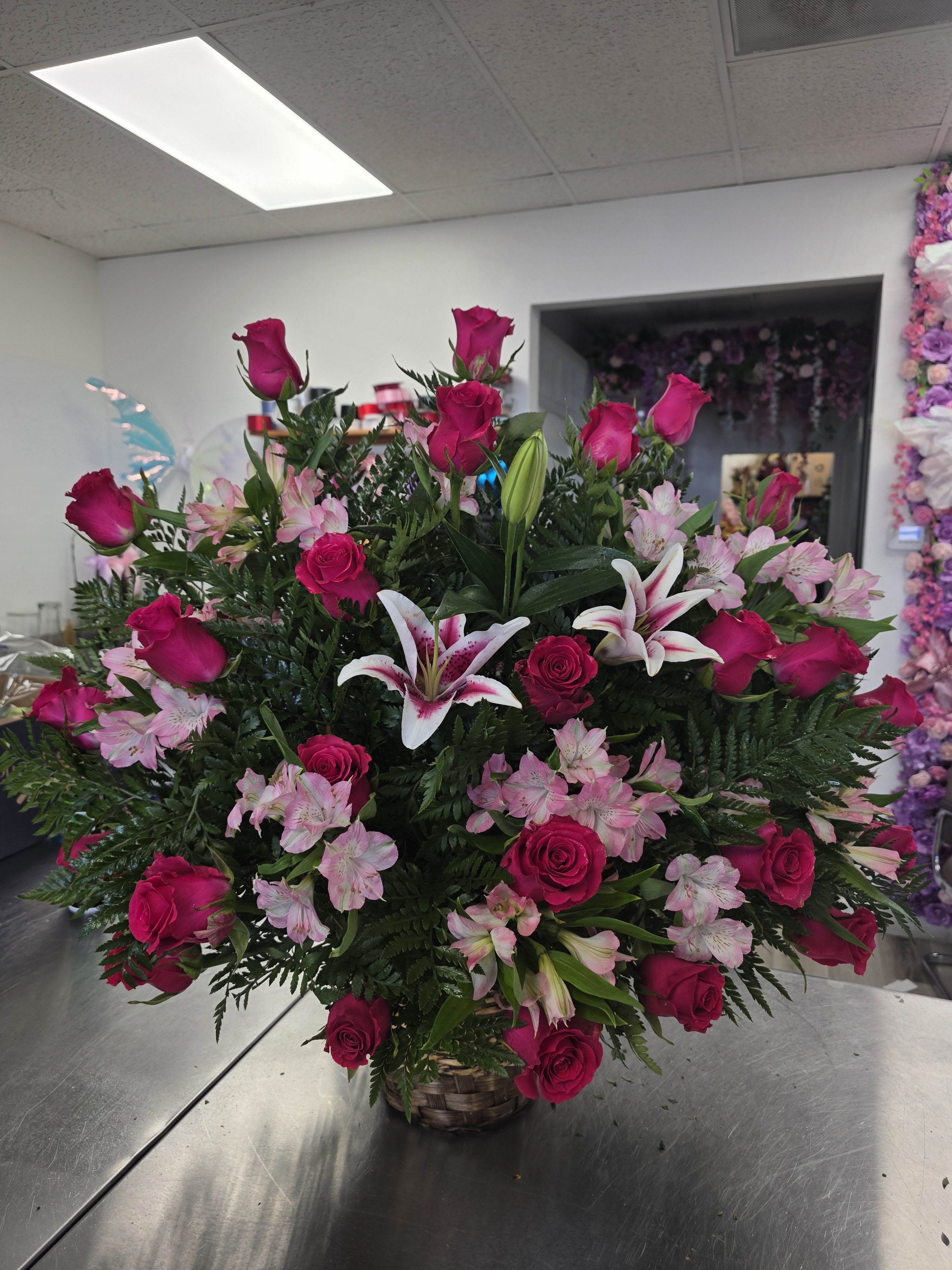 Basket arrangement of hot pink roses, pink lilies, and pale pink flowers