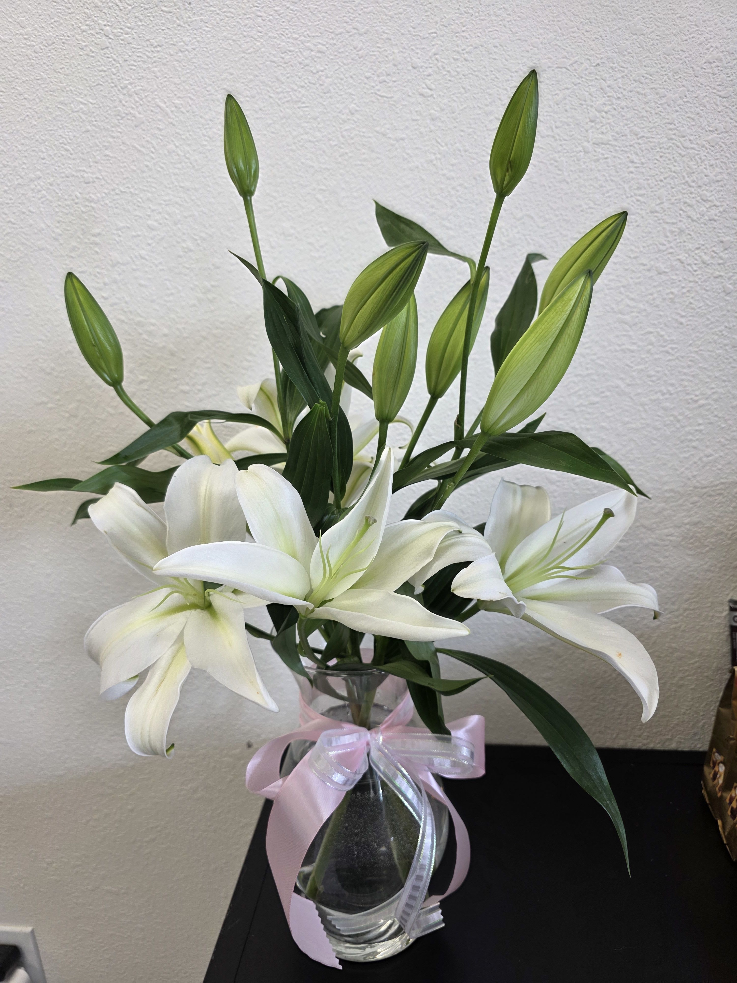 White lilies in a clear glass vase with a pink ribbon
