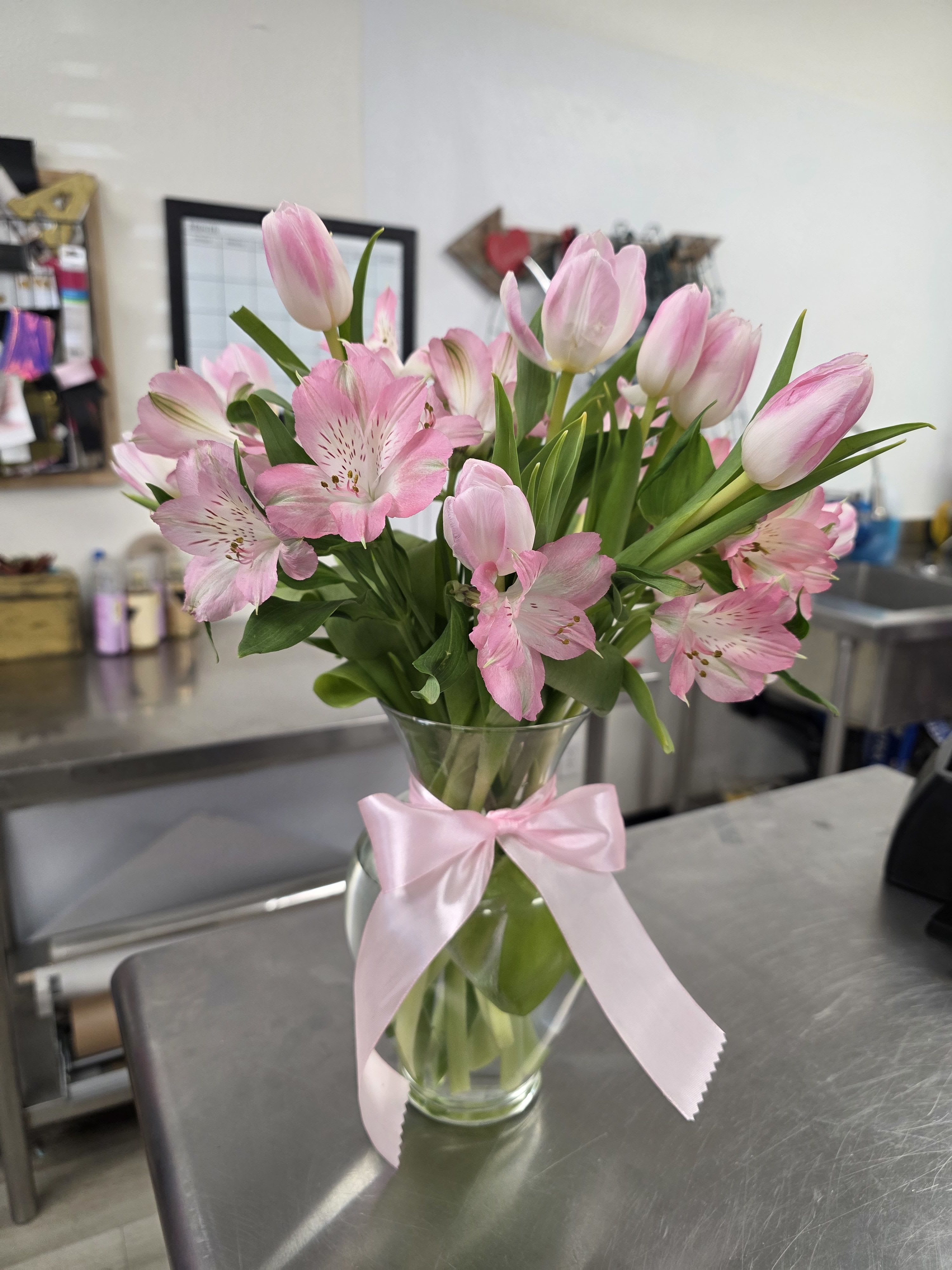 Pink tulips and alstroemeria in a glass vase with a pink ribbon