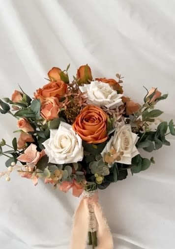 Bouquet of orange and white roses with greenery and a peach ribbon