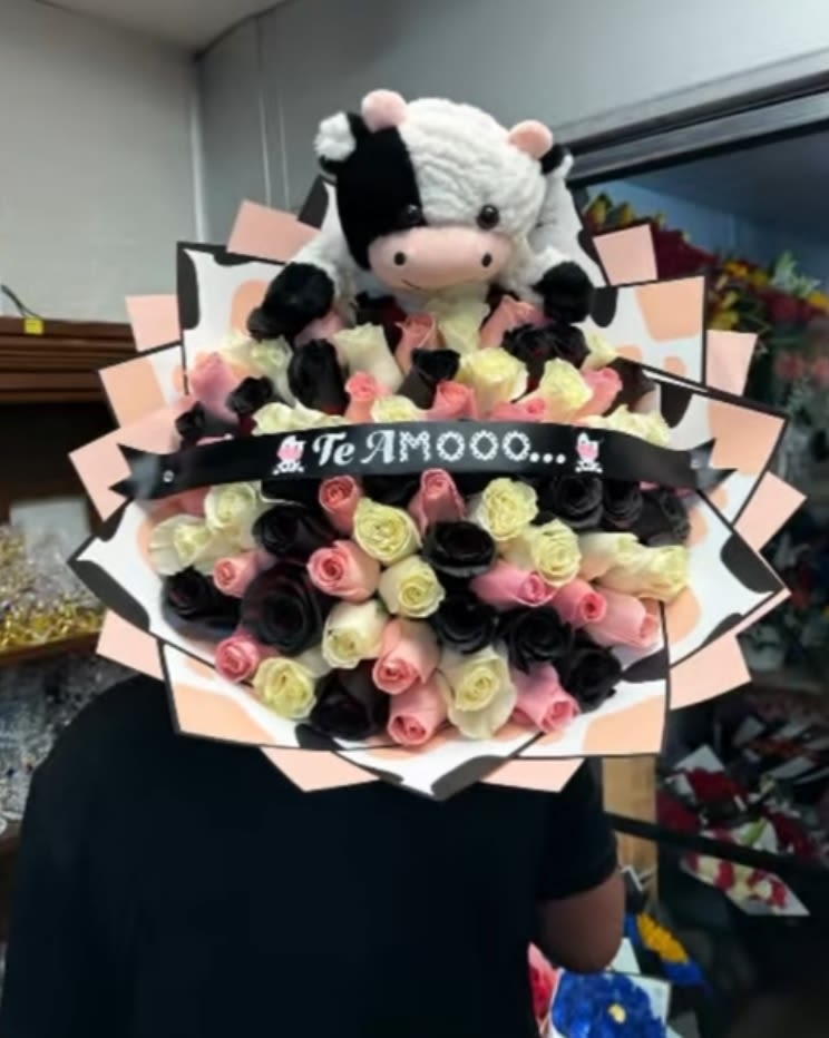Bouquet of pink, cream, and black roses with a plush cow topper