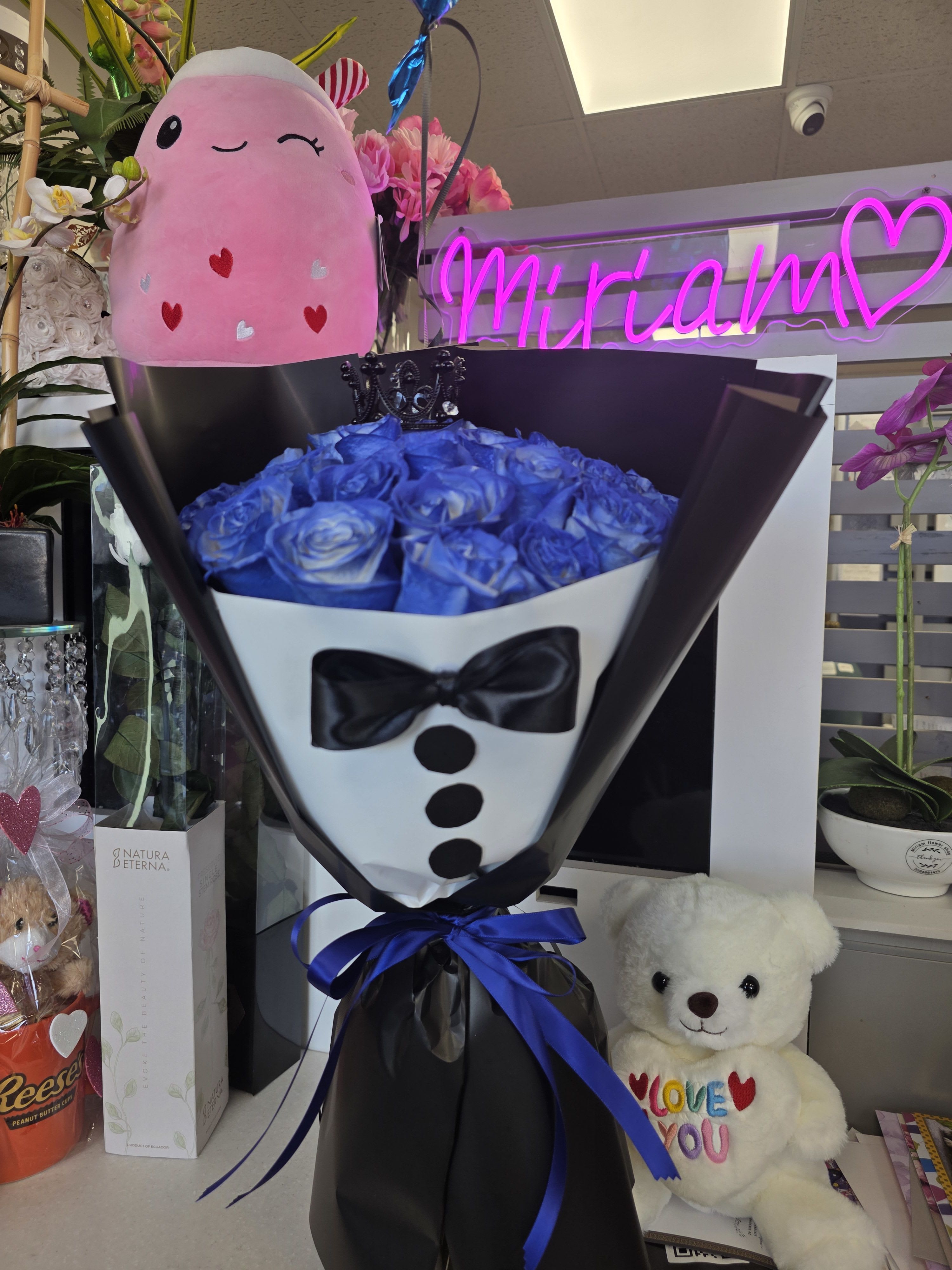 Bouquet of blue roses wrapped like a tuxedo with a teddy bear nearby