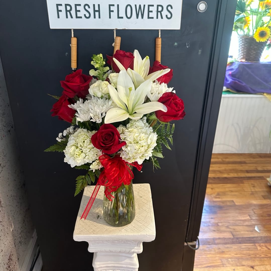 Red roses and white lilies arranged in a glass vase with a red ribbon.