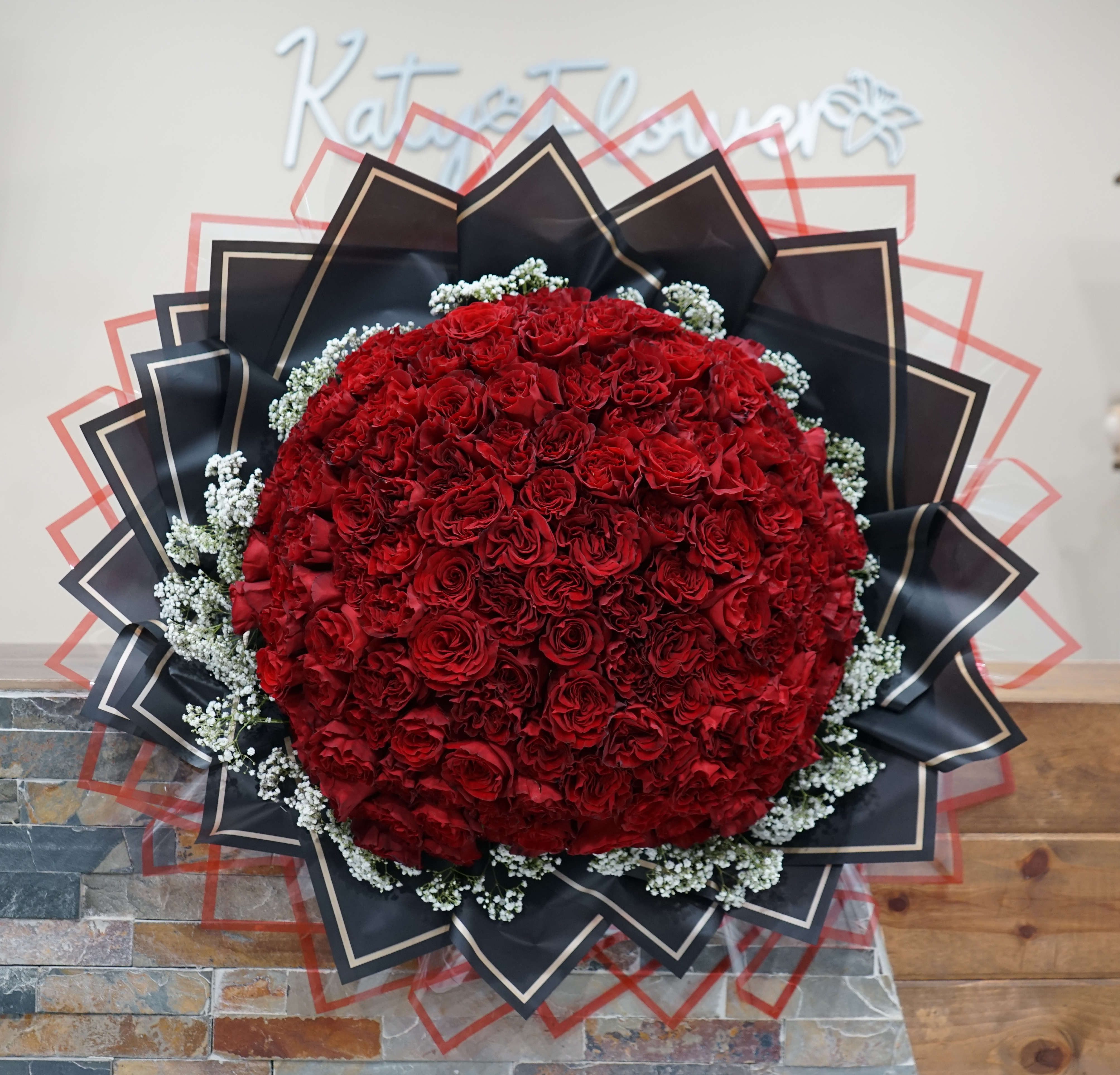 Large round bouquet of red roses with black wrapping and white filler flowers