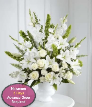 White floral arrangement in a white pedestal vase with tall green accents