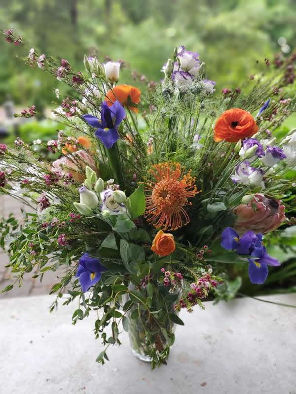 Mixed bouquet of orange, purple, and white flowers in a clear glass vase