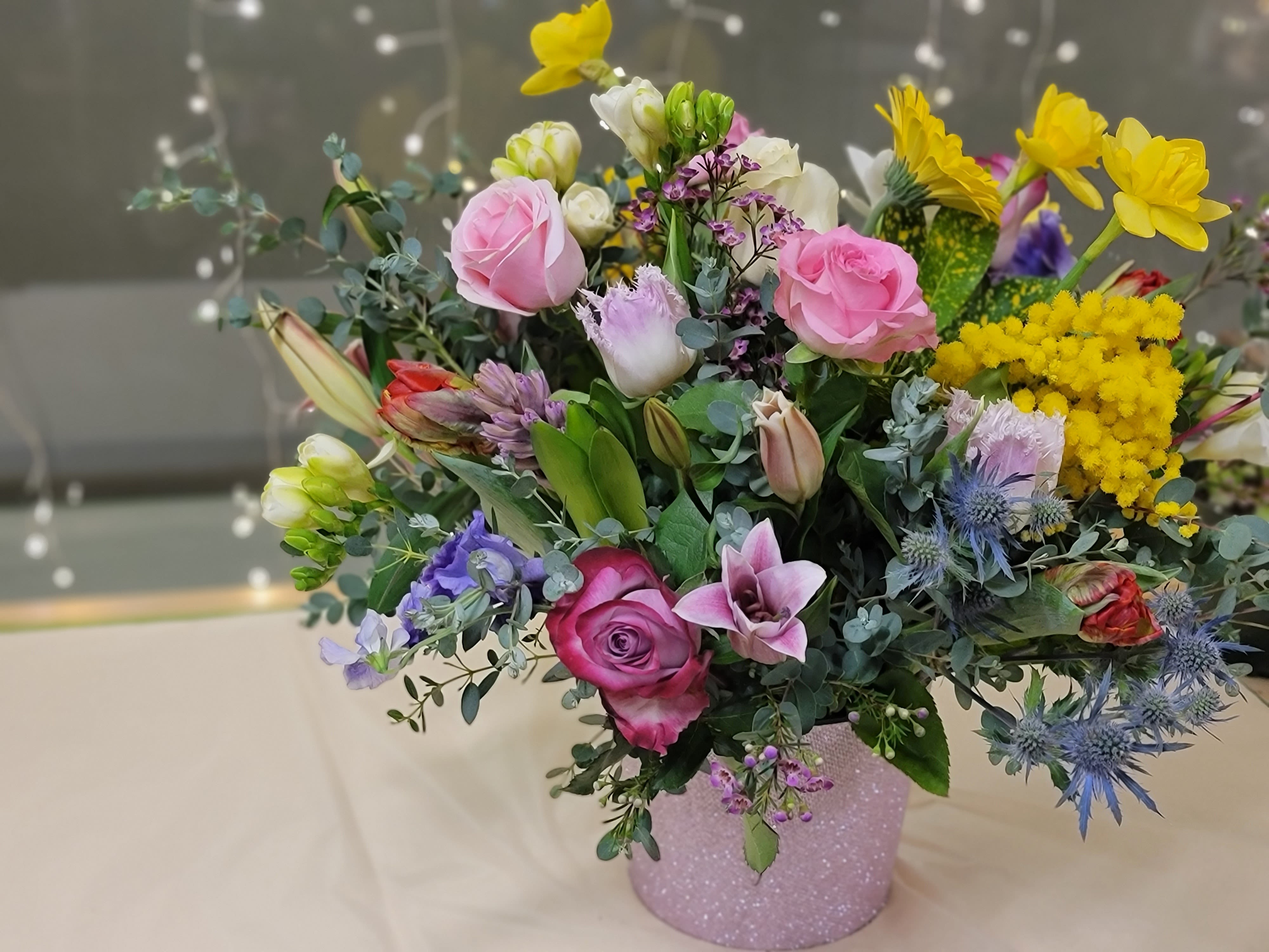 Mixed bouquet of pink, yellow, and purple flowers in a glittery vase