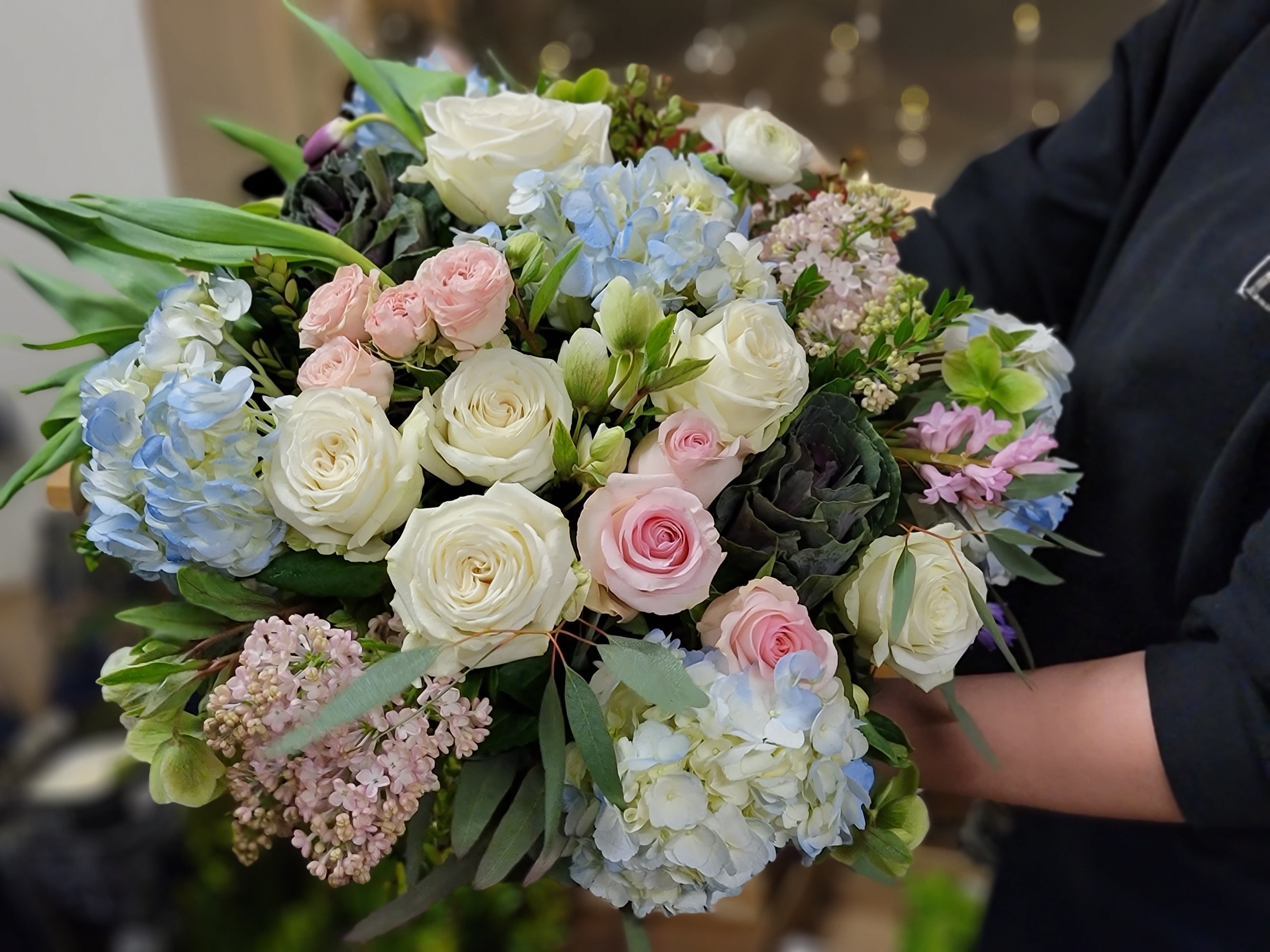 Handheld bouquet of white and pastel pink roses with blue hydrangeas