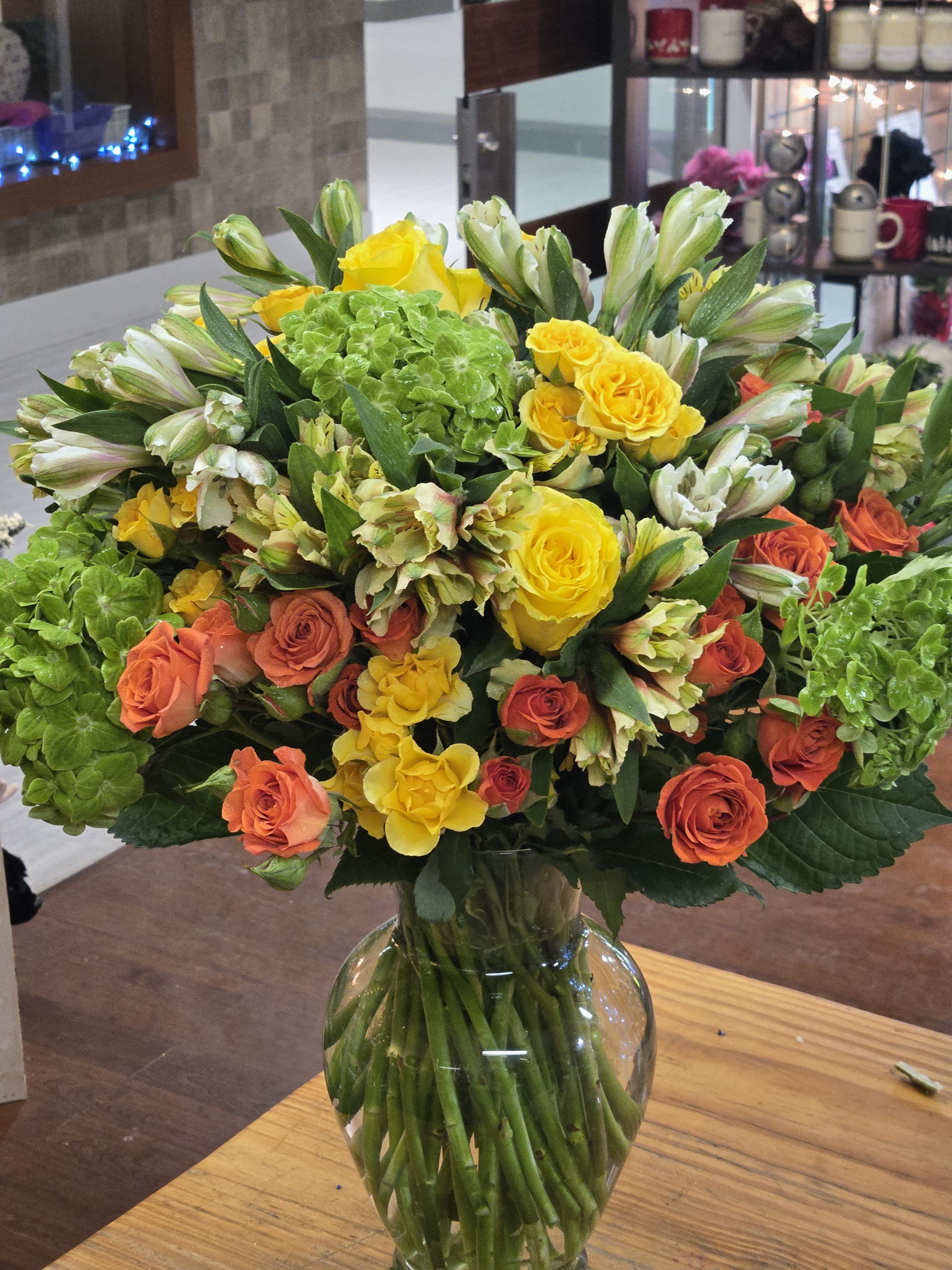 Bouquet of yellow and orange roses with green hydrangeas in a glass vase