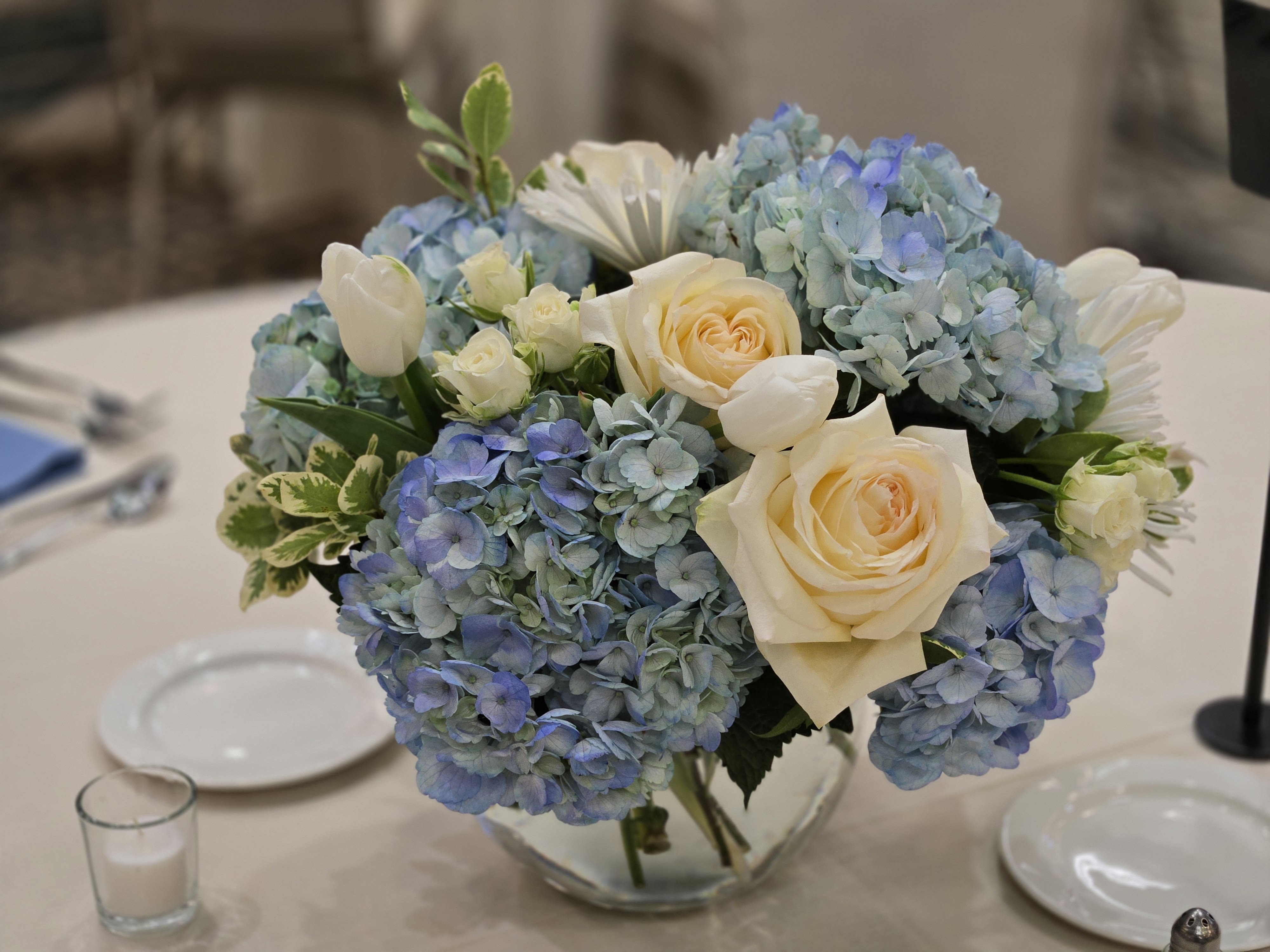 Blue hydrangeas and cream roses in a clear glass vase