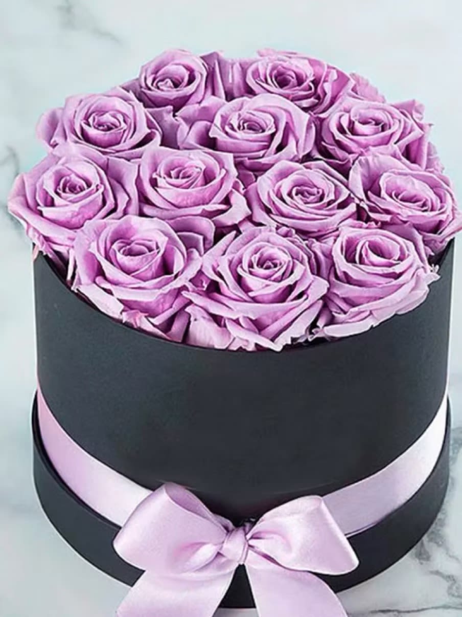 Lavender roses arranged in a black round box with a pink ribbon