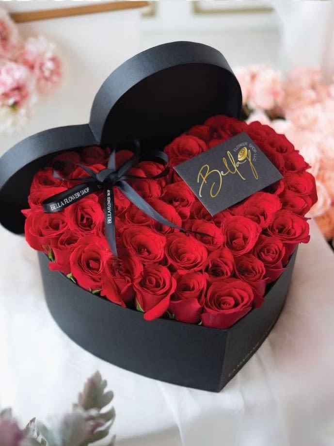 Heart-shaped box filled with red roses and tied with a black ribbon