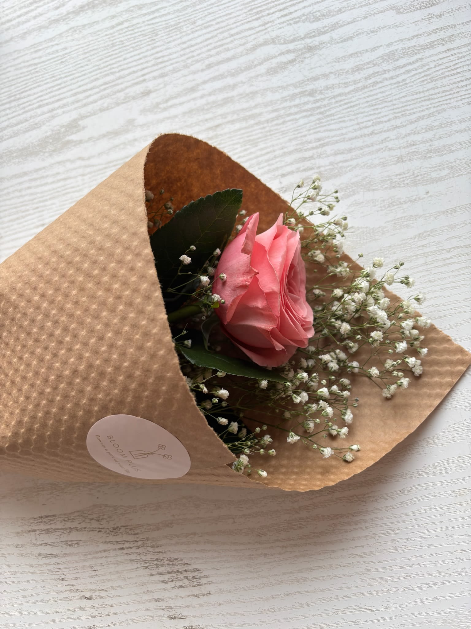 Single pink rose wrapped in brown paper with baby's breath