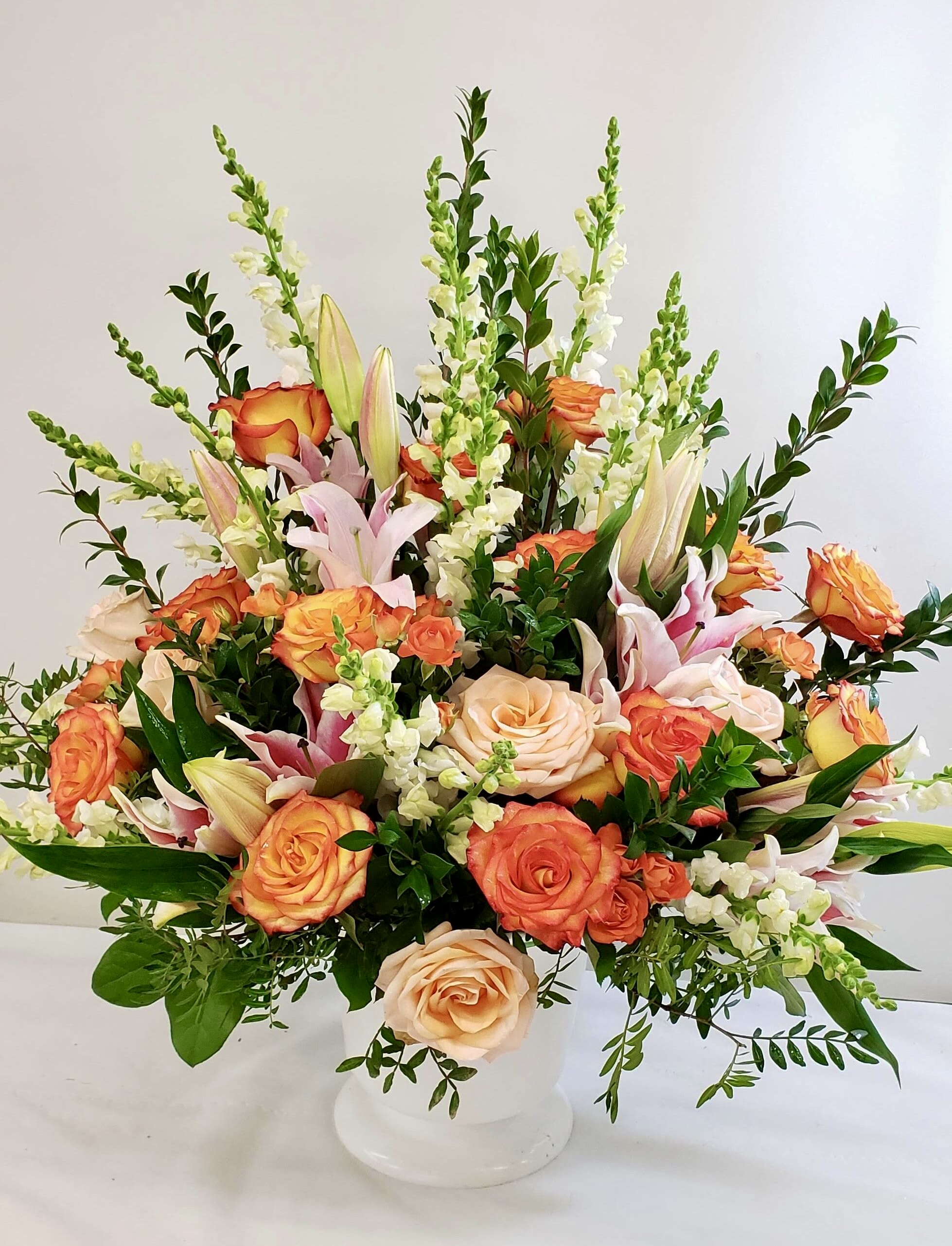 Mixed bouquet of orange and peach roses with white lilies in a white vase