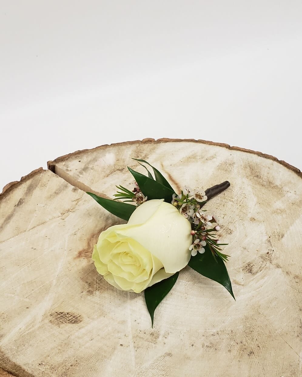 White rose boutonniere with small white blossoms on a wood slice