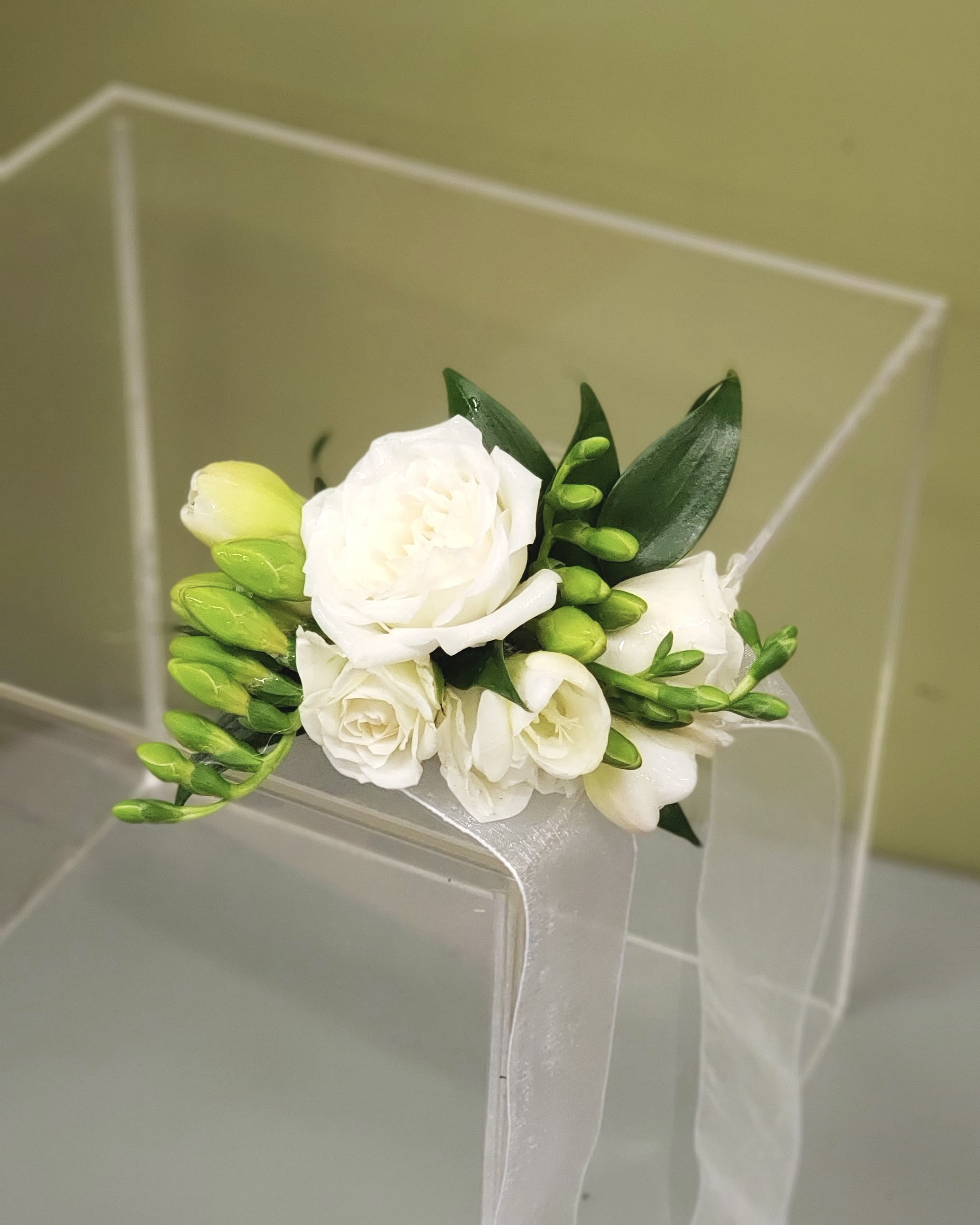 White floral wrist corsage with green buds and ribbon