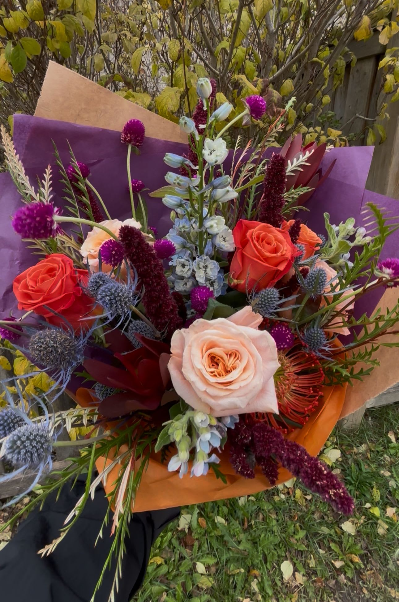 Hand-tied bouquet of coral and blush roses with purple accents