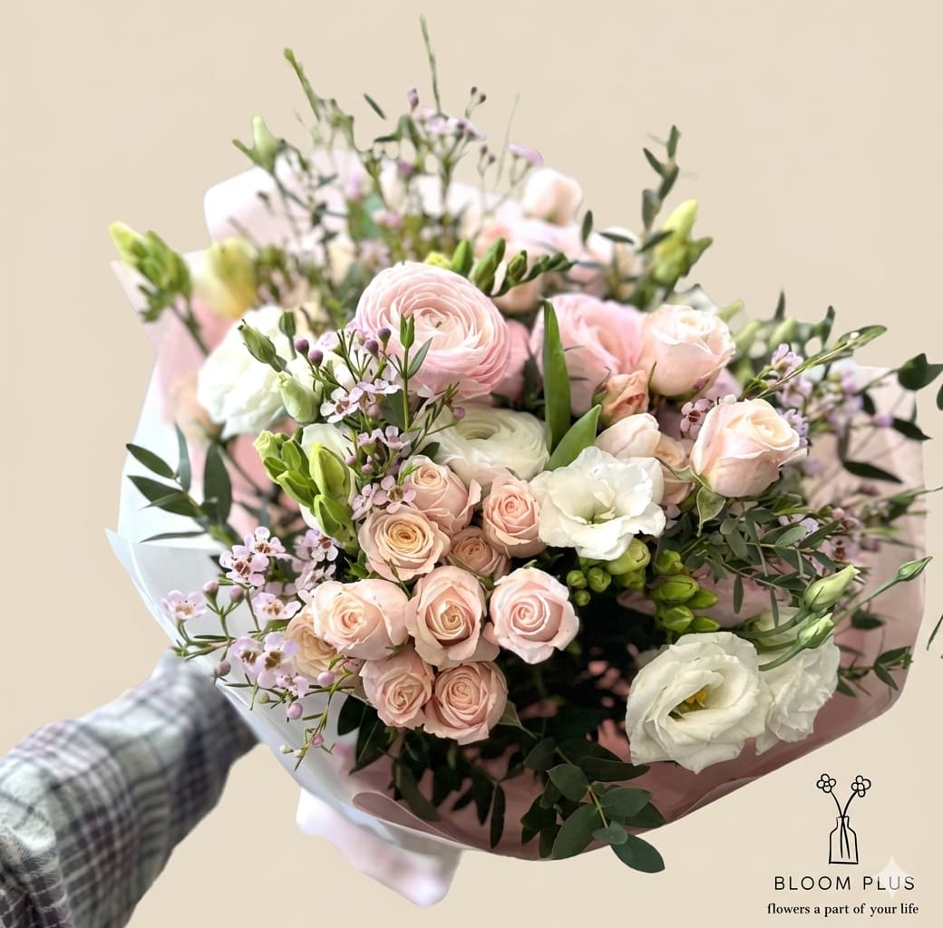 Handheld bouquet of pale pink and white flowers wrapped in pink paper