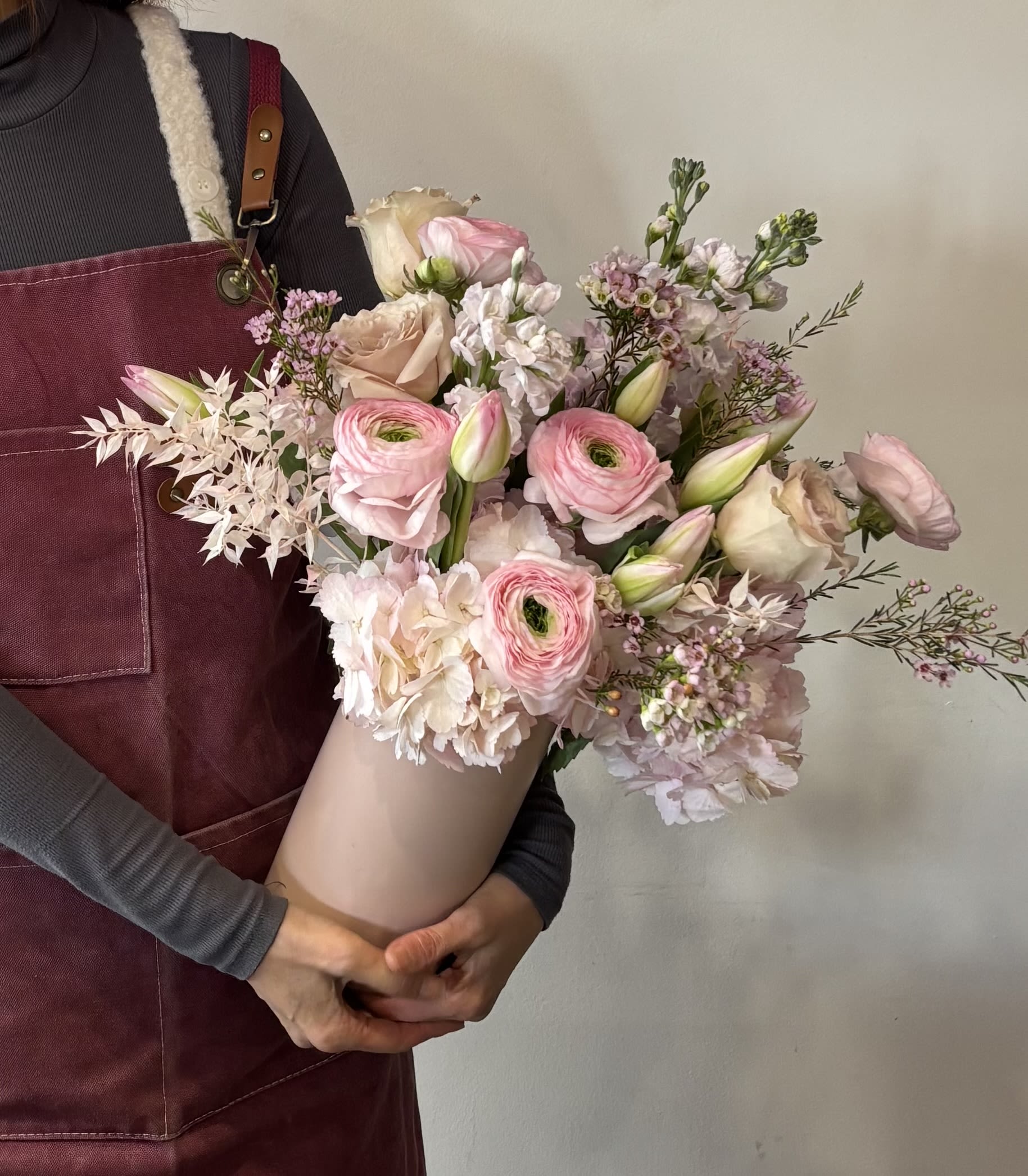 Handheld bouquet of pink and cream flowers wrapped in paper