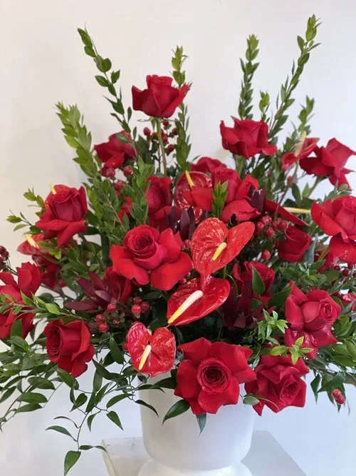 Red roses and anthuriums arranged in a white vase