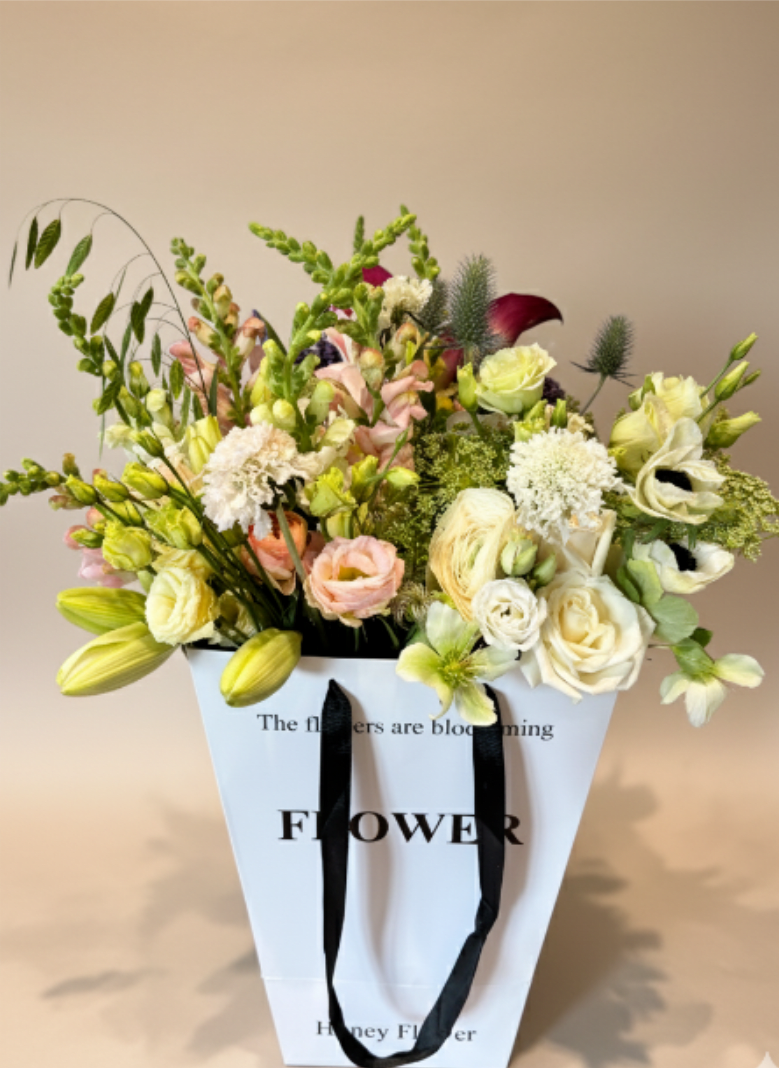 BP6 - Blush &amp; Bloom Flower Bag - It features a sophisticated gathering of cream and blush Lisianthus, fragrant Stock, and lush roses. Delicate and stylish, it’s the ideal gesture for celebrating moments large and small.  Seasonality:  •	Anemones: Peak late Winter through Spring.  Please note: Each piece is unique and uses the freshest seasonal blooms available. While substitutions may occur, we always maintain the beautiful blush and white color palette. 